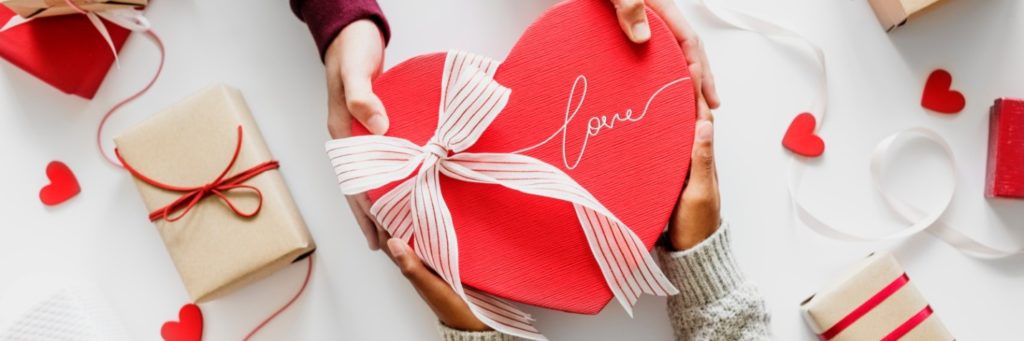 a man and woman holding a heart-shaped box with ‘love’ written on it